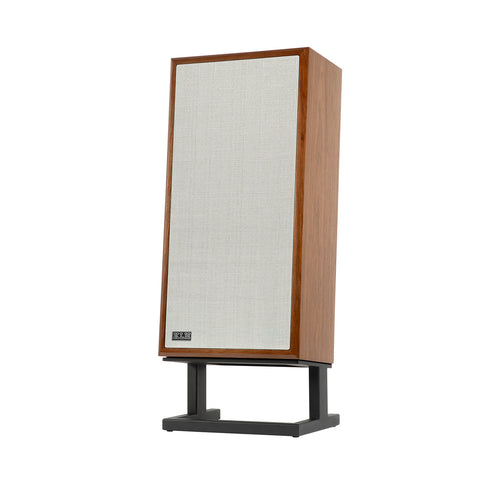 A floor-standing bookshelf speaker by B&G, featuring a warm medium-brown wood grain cabinet, a large off-white fabric grille, and a black metal stand, shown against a plain white background.